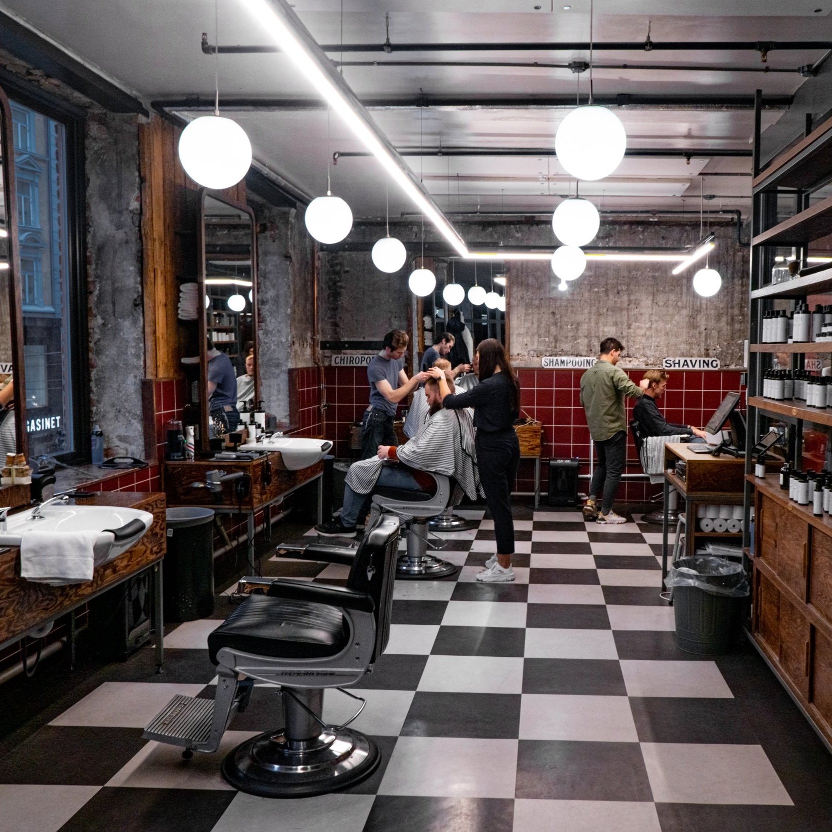 Interiør av klassisk barbersalong med sjakkrutemønster på gulvet, røffe betongvegger og kunders om får behandling